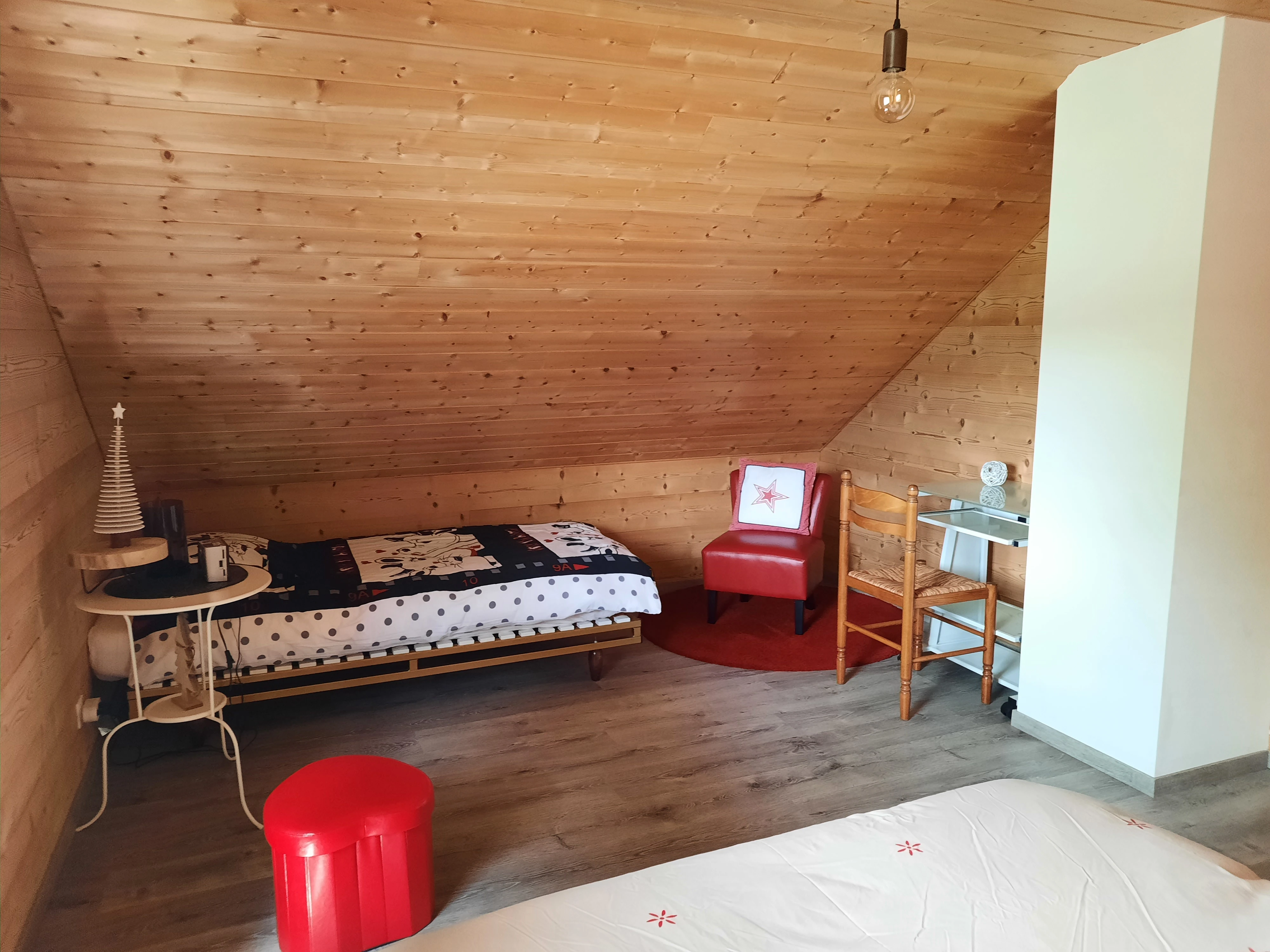 Chambre mansardée avec lit simple et fauteuil rouge